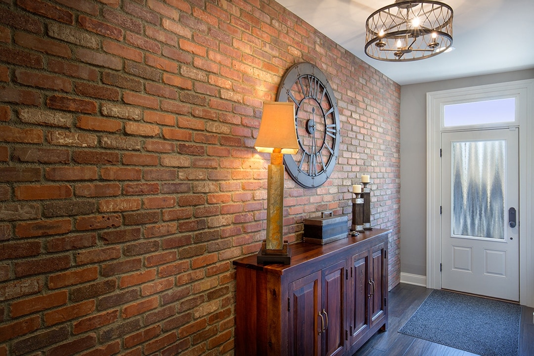 A renovated interior of a front entrance to a home. A new brick wall, door, and lighting is seen.