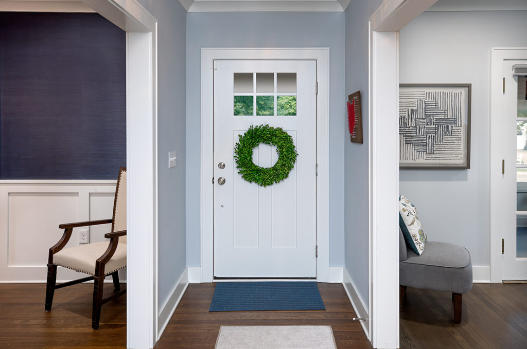 An Epic Group front door. The door is white and wood with silver hardware. The silver hardware offers a sleek and modern look to the home's entry. There is a green wreath on the door below the window on upper part of the door.