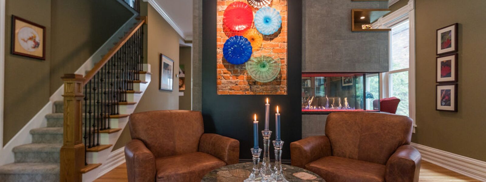 Modern living room renovation in a historic Victorian Village Columbus home, featuring a see-through fireplace, leather chairs, bold wall art, and updated staircase design.