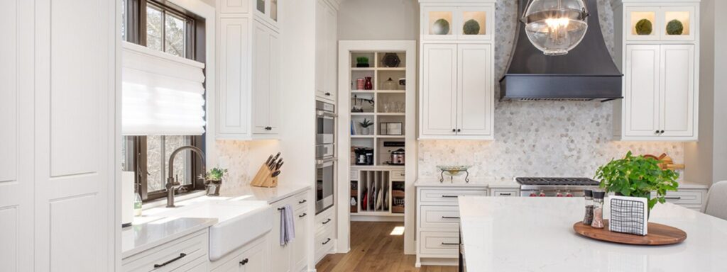 Bright and airy modern kitchen layout featuring white cabinetry, a large central island, black accents, and a walk-in pantry with open shelving.